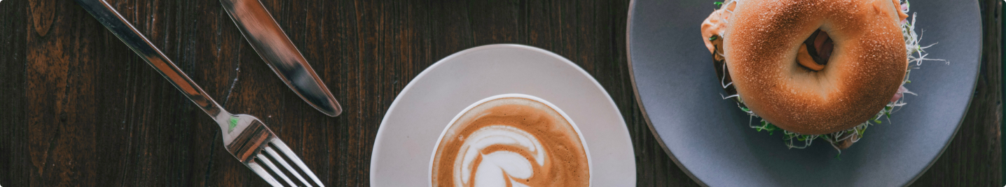 Eine Tasse Cappuccino und ein belegter Bagel stehen auf einem Holztisch