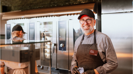 Küchenpersonal steht hinter der Ausgabe und lächelt in die Kamera